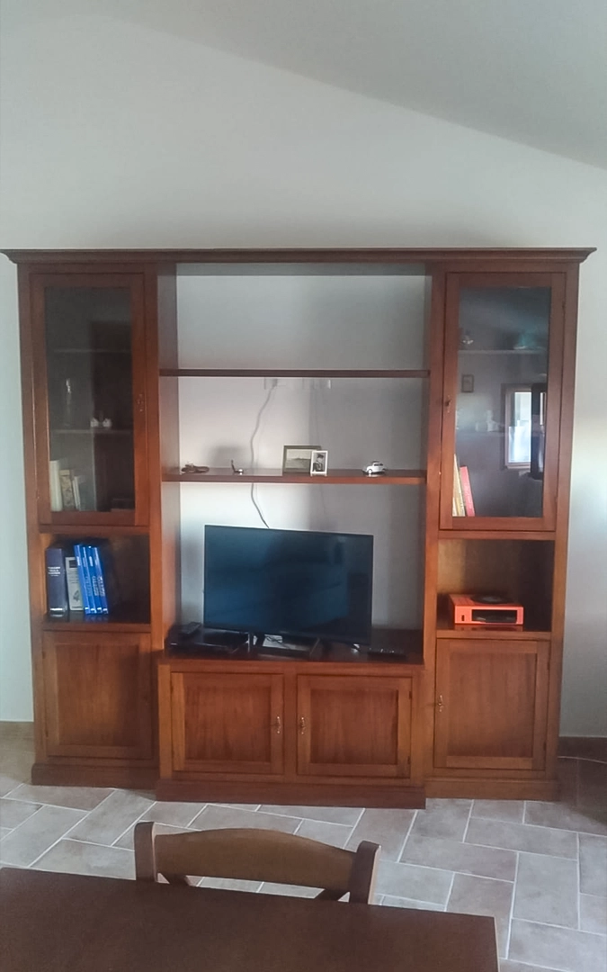 Parete attrezzata in legno arte povera noce scuro con finitura Bassano, completa di mobile porta TV, vetrine laterali e vani contenitori.